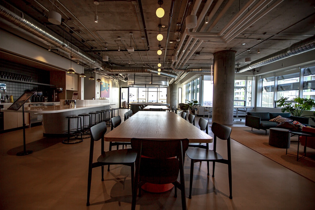 Ett samtida coworking-utrymme med ett stort gemensamt träbord, caféområde och loungemöbler.